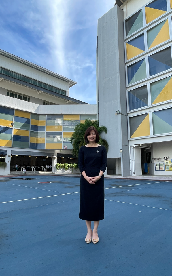 Woman in a black dress standing on a blue court in front of a colorful school building with yellow and blue panels.